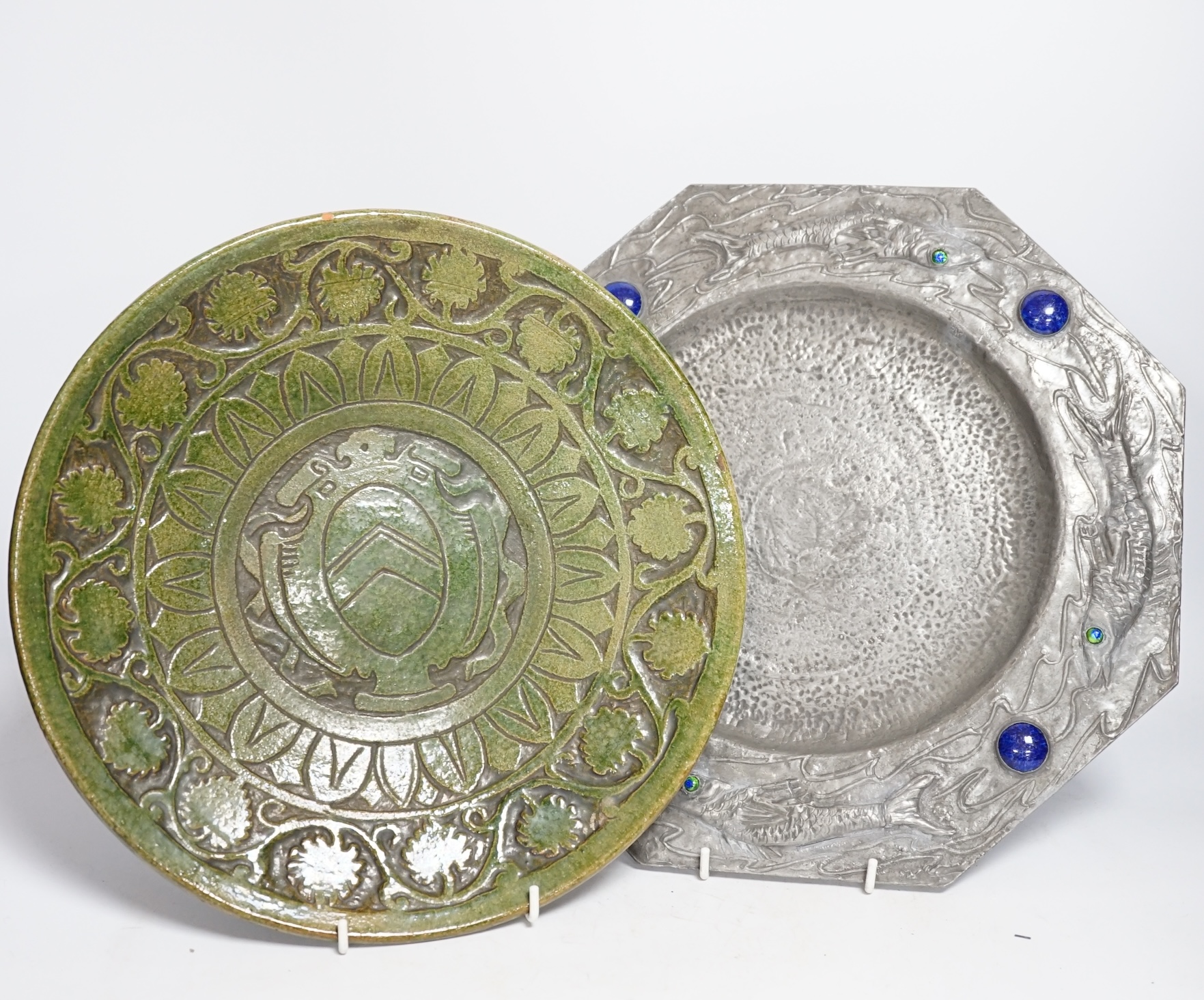 An Arts and Crafts style pewter fish plate with ceramic insets and glass eyes together with a pottery armorial charger, pewter charger 35cm wide